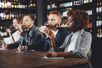 African Woman and caucasian man sommeliers tasting red wine and taking notes at degustation notepad