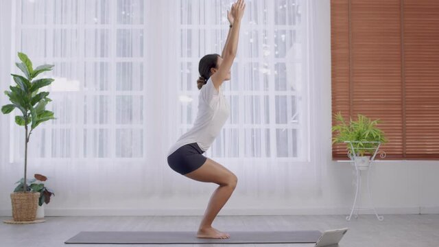 Standing in Parsvakonasana stance, Side Angle exercise, Asian lady doing yoga, attractive female in grey sportswear, working out at home.