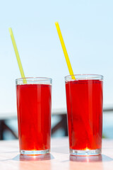 Two glasses with berry juice and strawberries on the table of a street cafe against  background of the sea.
