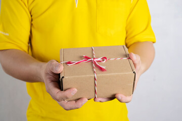 Brunette man holding a paper box in both hands wearing a yellow polo shirt with a white background.