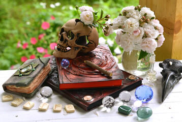Vintage summer still life with old witch book for fortune telling, skull, crystals and runes on ritual table.