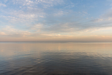 Fototapeta na wymiar Calm evening sea surface with clear blue sky. Evening seascape.