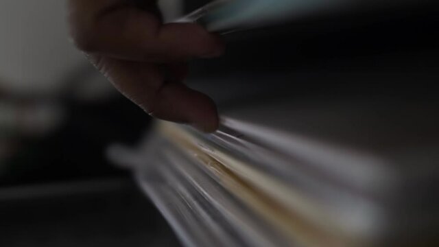 Close up vertical video of a DJ's hand as he flips open the lid of his vinyl box, revealing his collection of albums and begins searching for his preferred track