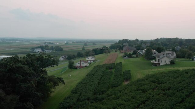 Aerial of drone flying in midair above orchard and homes. Sun on horizon. Unmanned flight vehicle.