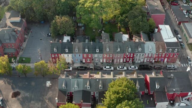 Descending aerial on colorful row homes. Cars parked on street by houses. Urban American city, town. Residential district.