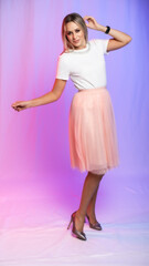 beautiful woman portrait in studio posing. A girl in a white blouse, a T-shirt and a pink, peach pleated skirt laughs, spins, dances. colored, crimson purple background. holiday, new year, birthday