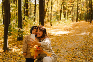 Fototapeta na wymiar Mom and son take a selfie on the phone in the autumn forest. People use technology. Autumn outdoor activity for family with kids. Happy mother's day. Family day. Autumn day. Happy family leisure.