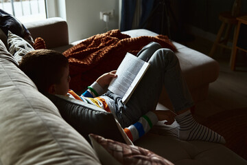 Obraz premium Young boy reading book on the sofa at home