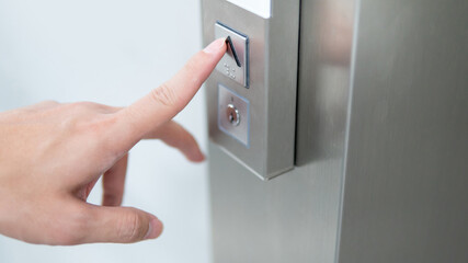 Naklejka premium Male forefinger pressing on button up in front of the elevator (lift) in office building. Mechanical engineering concept