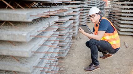 Smart Asian worker man or male civil engineer with protective safety helmet and reflective vest using digital tablet for project planning and checking material at construction site.