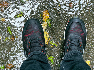 Beine in schwarzer Jeans mit nassen Schuhen in der Regenpfütze mit gelben Blätter. Herbst in Deutschland.