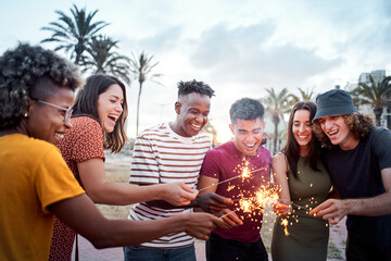 Group of friends smiling and having a good time around some sparklers. Mixed race youngsters enjoy spending time together in summer. Concept of friendship, free time, integration.