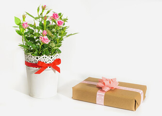 A bouquet of roses in a white vase and a gift in brown paper on a white background