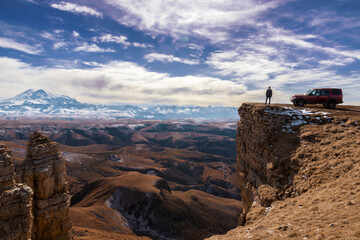 View of Mount Elbrus in autumn from the Bermamyt plateau, next to the silhouettes of a car and a...