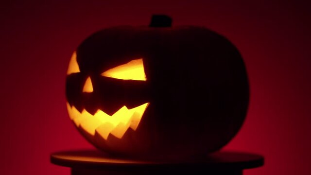 continuous looping rotation of a halloween pumpkin with carved teeth, eyes and nose, with a glowing fanar inside in the dark on a red background