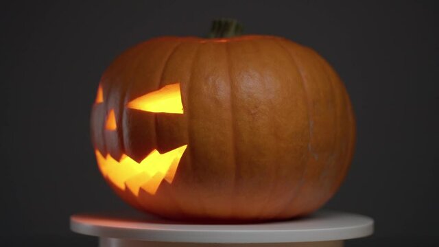 continuous looping rotation of halloween pumpkin with carved teeth, eyes and nose, with glowing fanar inside on dark background