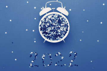 Fototapeta na wymiar Alarm clock and star shaped confetti on blue background. 2022