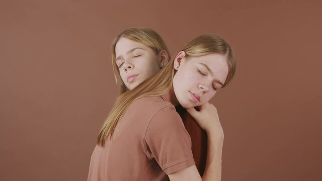 Tilt up shot of young twin sisters embracing against brown background