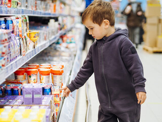cute toddler boy in casual clothes in market looking on yogurts