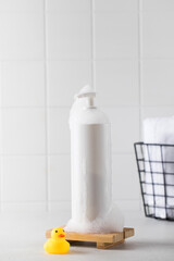 Bottle of organic cosmetic product covered with fluffy foam stands on white table