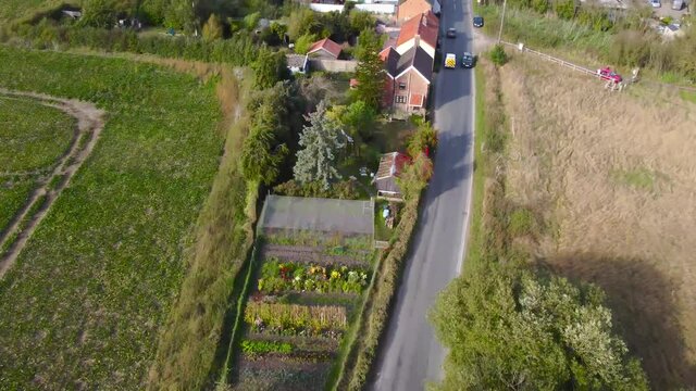 Flying over agricultural farmland area with road and houses at Norfolk, England - aerial drone shot