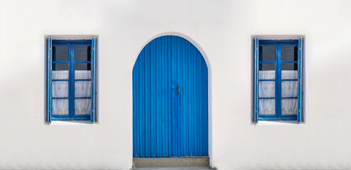 Blue wooden door on whitewashed wall windows with opened shutters and curtains background.