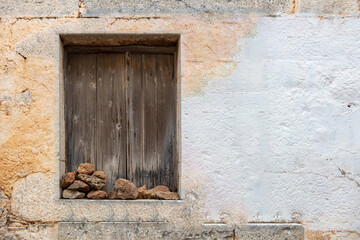 Aged window with wooden shutters stones on sill peeled cracked empty wall background. Copy space