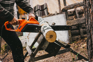 Man sawing a birch trunk with a chainsaw in the forest. Forester at work