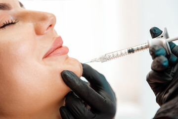 Cosmetologist in latex gloves makes with syringe injects of a botox. Woman getting injection at her...