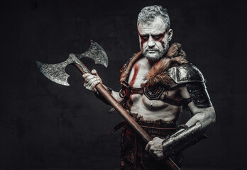 Serious fighter with naked torso armed with axe in studio