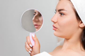 Rhinoplasty. A young beautiful woman holds a mirror with aquiline nose. Comparison of results...