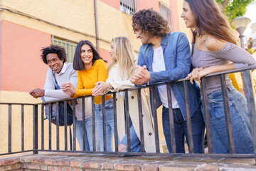 Multi-ethnic group of friends gathered in the street leaning on a railing.