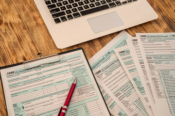 on  wooden table are tax forms 1040, calculator, laptop pen notebooks