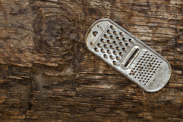 An old rusty kitchen grater on a rotting board with a knot.