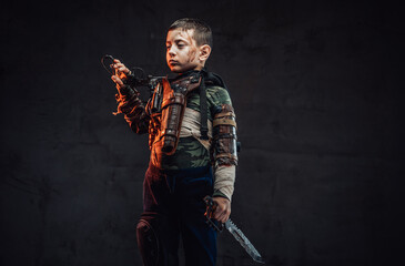 Preschool boy armed with knife and gun in dark background