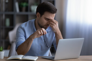 Unhappy stressed young male employee taking off eyeglasses feeling eyestrain, suffering from...