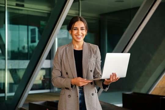Smiling businesswoman holding laptop out of office