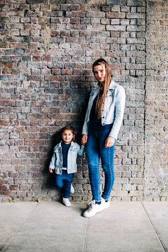 Mother and daughter standing together in front of brick wall