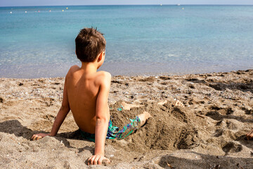 happy boy sits on a sandy beach near the sea and looks into the distance, vacation