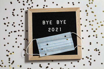 black letter board with text BYE BYE 2021 with small stars and mask on white background.