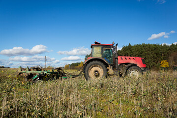 A farmer in a tractor, agricultural machinery, prepares the land with a cultivator. A modern red tractor in a field. Plowing a heavy tractor while cultivating agricultural work in a field with a plow.