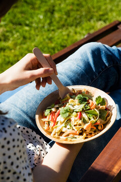 Mid section of young woman eating bowl of raw vegan pad thai