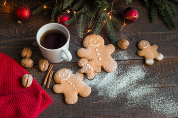 Gingerbread men on a dark wooden table sprinkled with powdered sugar with New Year's decor and a cup of tea.