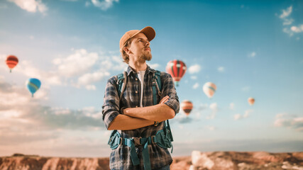 Portrait of a Young Handsome Tourist Posing with Backpack on Top of a Rocky Canyon Valley. Adventurous Male Backpacker on a Hiking Journey Trip. Hot Air Balloon Festival in Mountain National Park.