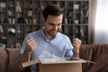 Happy young man feeling excited of getting wished item, enjoying unpacking huge carton box,...