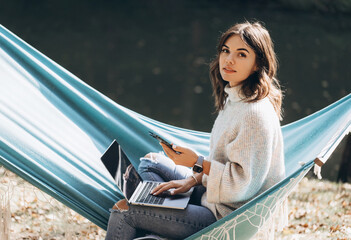 Beautiful smiling girl working with laptop in the park on a hammock