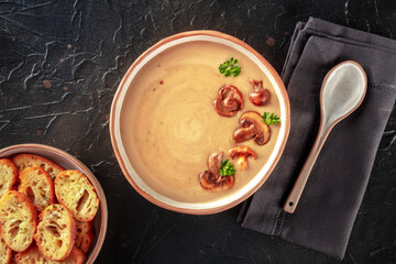 Mushroom soup in a rustic bowl with toasted bread, shot from the top on a black slate background
