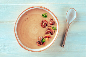 Mushroom soup, garnished with parsley, overhead shot on a wooden background with a spoon