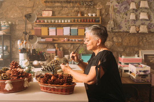 Mature female painter painting pine cone at workshop