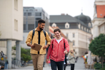 Young man with Down syndrome and his mentoring friend walking and talking outdoors